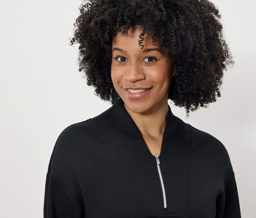 Portret uśmiechniętej kobiety z fryzurą afro w czarnej bluzie na zamek błyskawiczny.