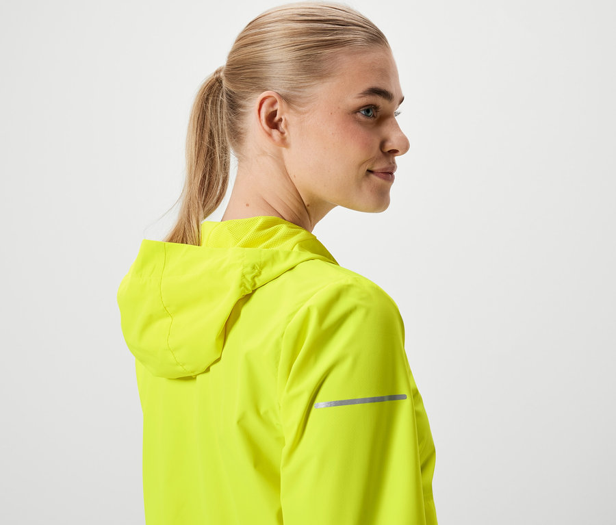 Kobieta o blond włosach związanych w kucyk, ubrana w neonowo żółtą kurtkę z kapturem.