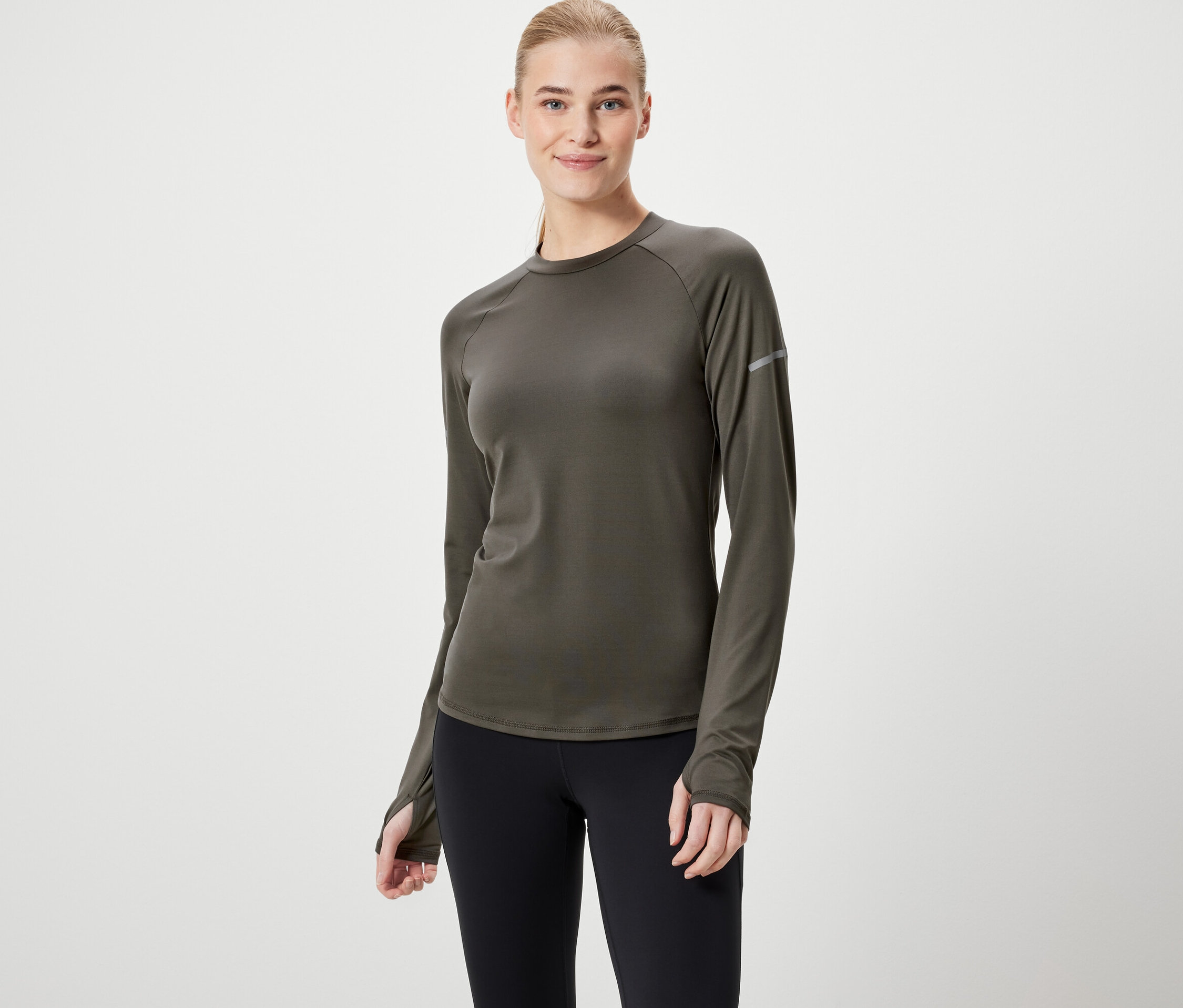 Kobieta ma na sobie oliwkowozieloną koszulkę z długim rękawem i czarne legginsy.