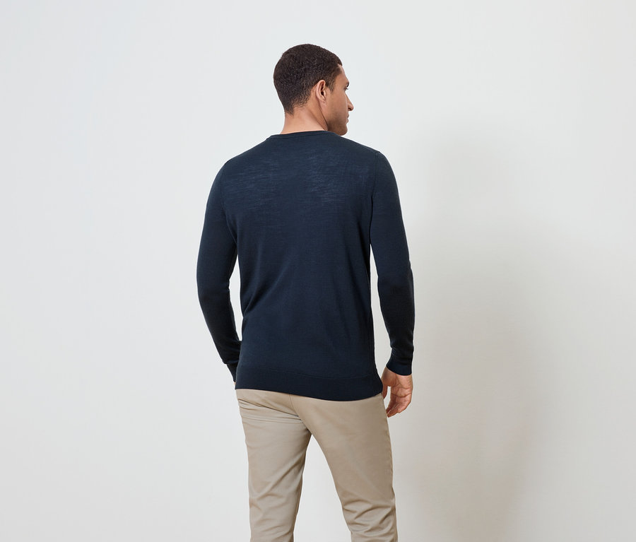 Mężczyzna od tyłu, ubrany w granatowy sweter i beżowe spodnie.