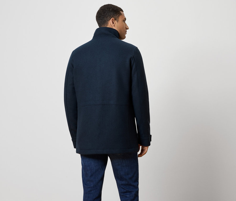 Mężczyzna od tyłu, ubrany w granatowy płaszcz i dżinsy.