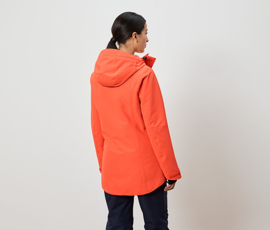 Kobieta tyłem do kamery ma na sobie pomarańczową kurtkę z kapturem.