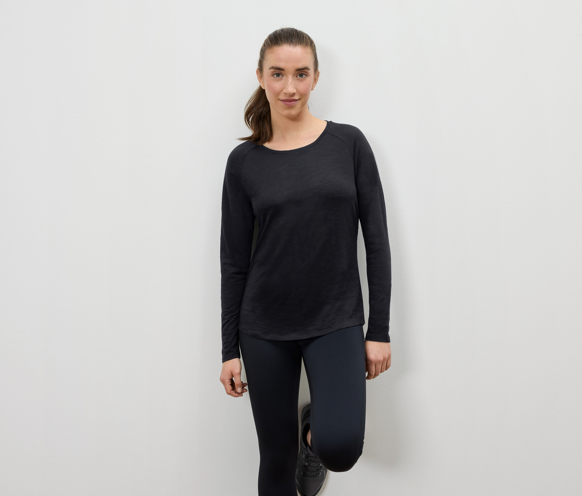 Kobieta w czarnym stroju sportowym oparta o ścianę.