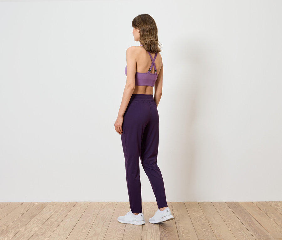 Kobieta widziana od tyłu, ubrana w fioletowy stanik sportowy i ciemnofioletowe spodnie.