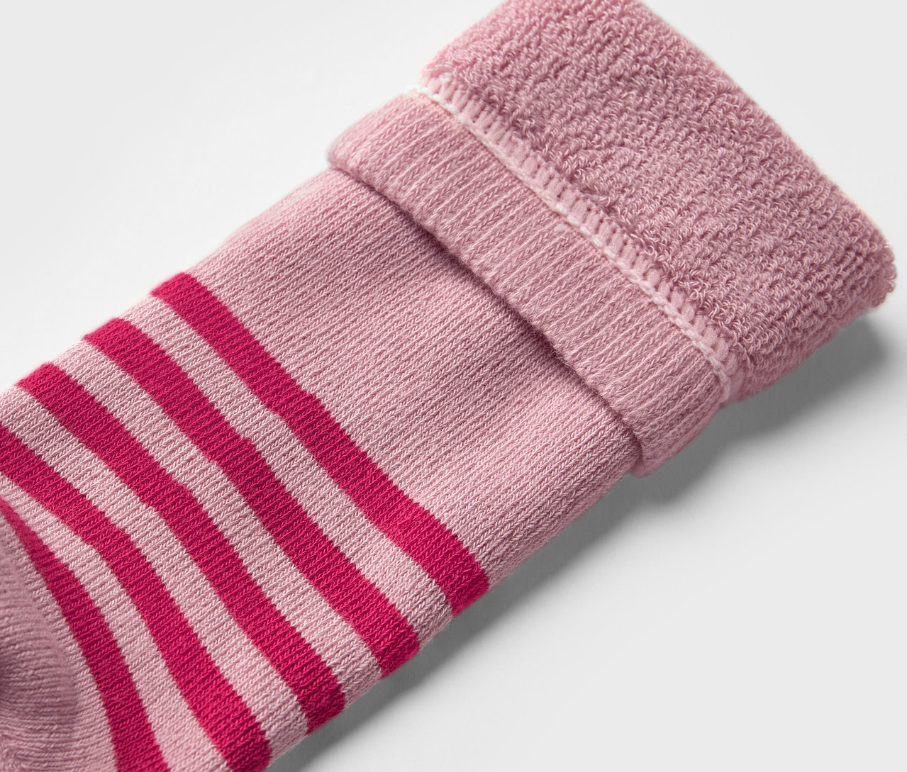 Zbliżenie na dziecięcą skarpetę do kaloszy (2 pary, w kwiatki). Skarpeta jest różowa z czerwonymi paskami i ma wywinięty brzeg.