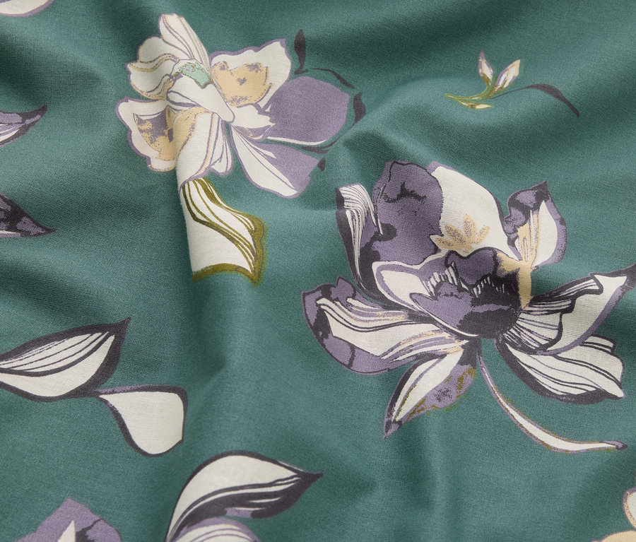 Zbliżenie tkaniny we wzory kwiatowe w odcieniach zieleni, fioletu i kremu.