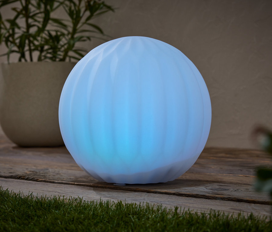 Niebieska kula świeci na drewnianej powierzchni obok rośliny doniczkowej.