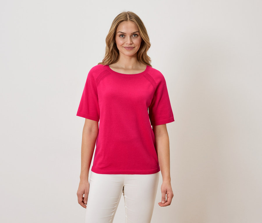 Kobieta ma na sobie różowy T-shirt i białe spodnie.