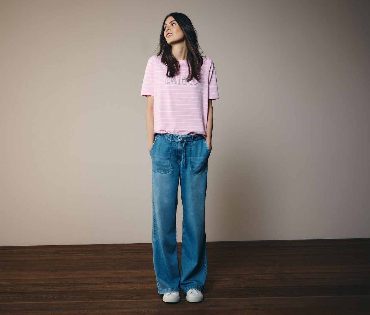 Kobieta z rękami w kieszeniach nosi koszulkę CECIL w różowe paski i dżinsy.