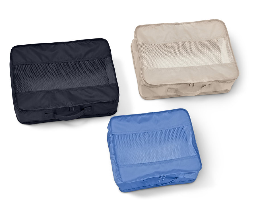 Trzy prostokątne organizery do walizek z siatkowymi okienkami w kolorze granatowym, beżowym i niebieskim leżą na białym tle.