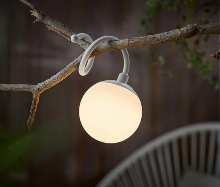 Biała, kulista lampa zwisa z gałęzi.