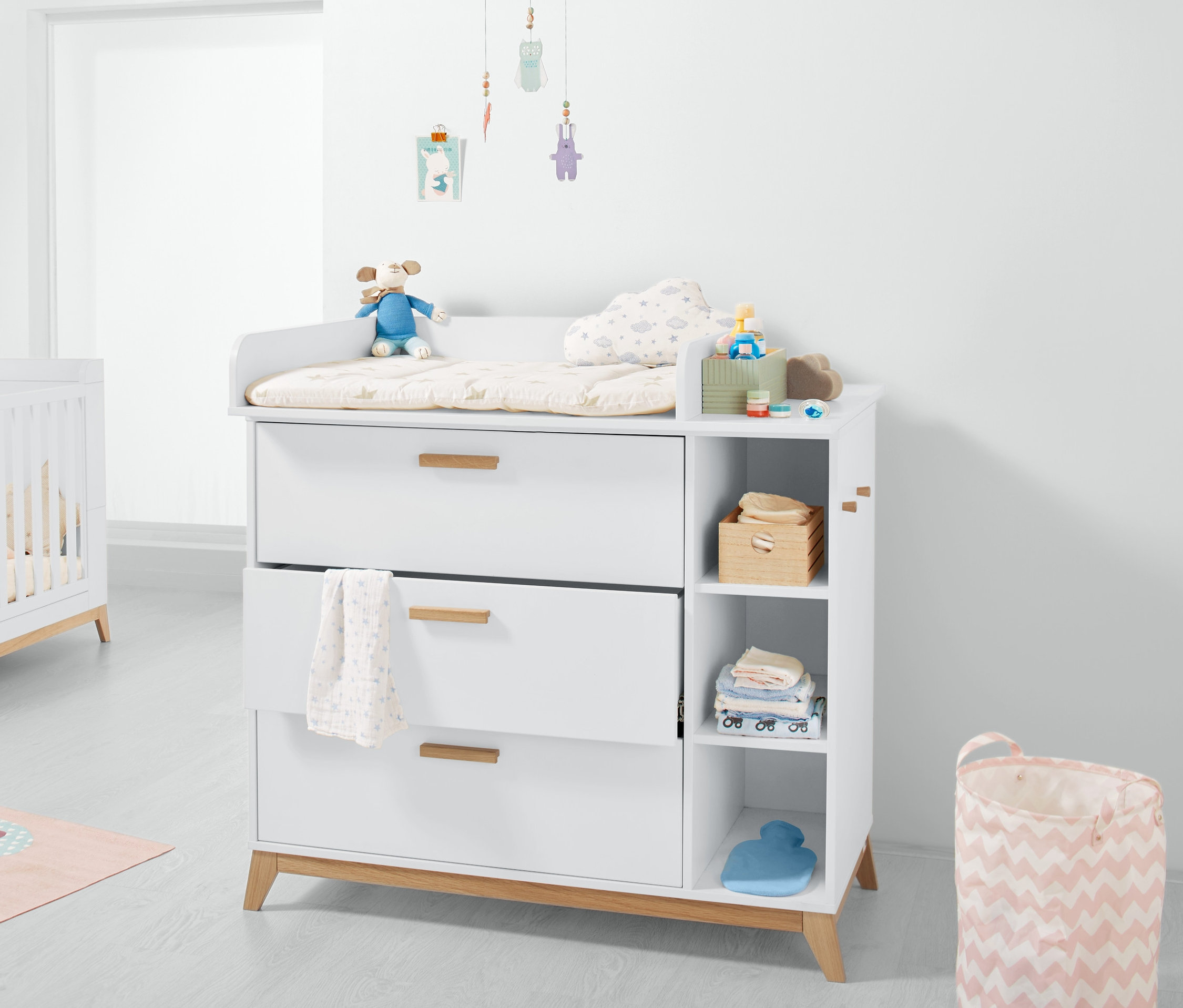 Biała komoda z przewijakiem, trzema szufladami i otwartymi półkami.