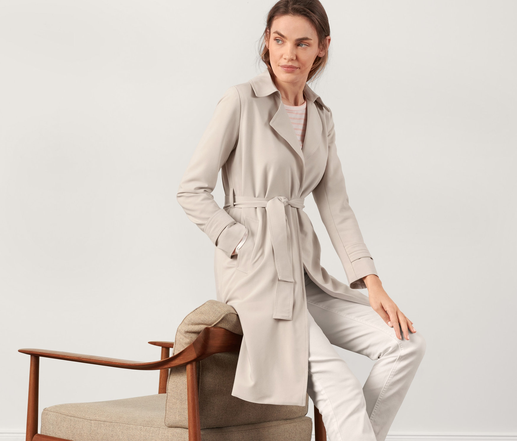 Kobieta siedzi na krześle i ma na sobie beżowy trencz.