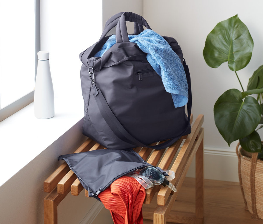 Torba sportowa leży na drewnianej ławce obok okna. Z torby wystaje niebieski ręcznik.