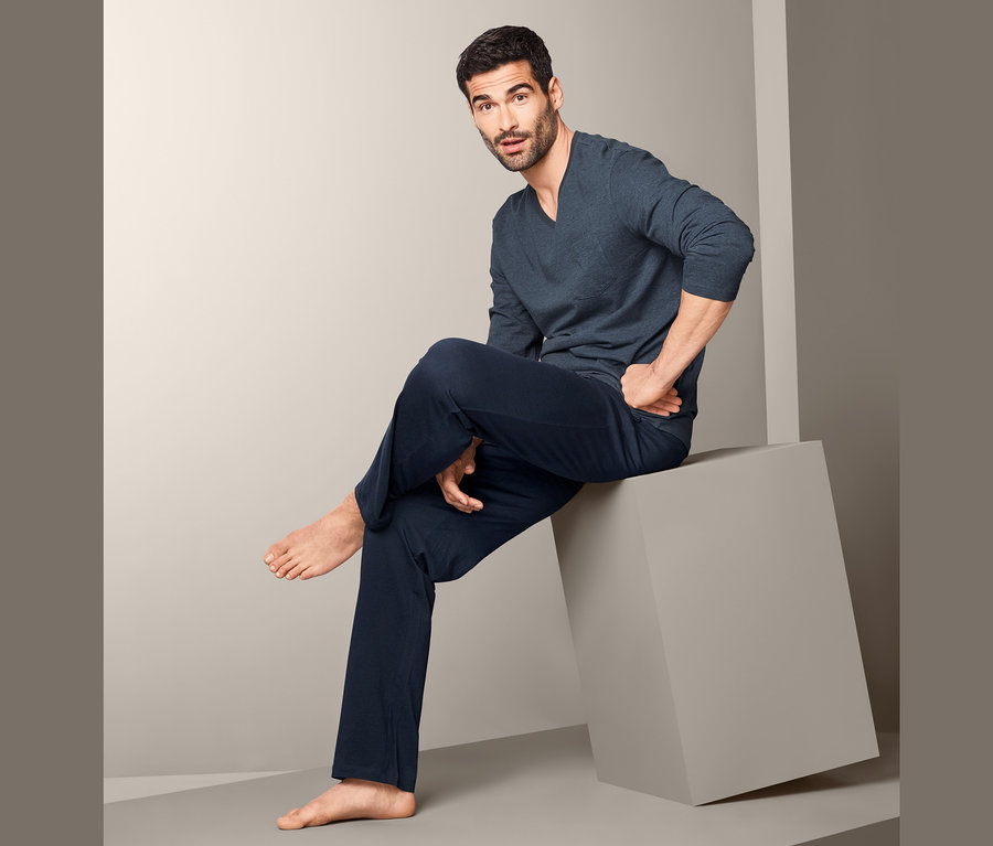 Mężczyzna siedzi na szarym sześcianie i ma na sobie męską piżamę.