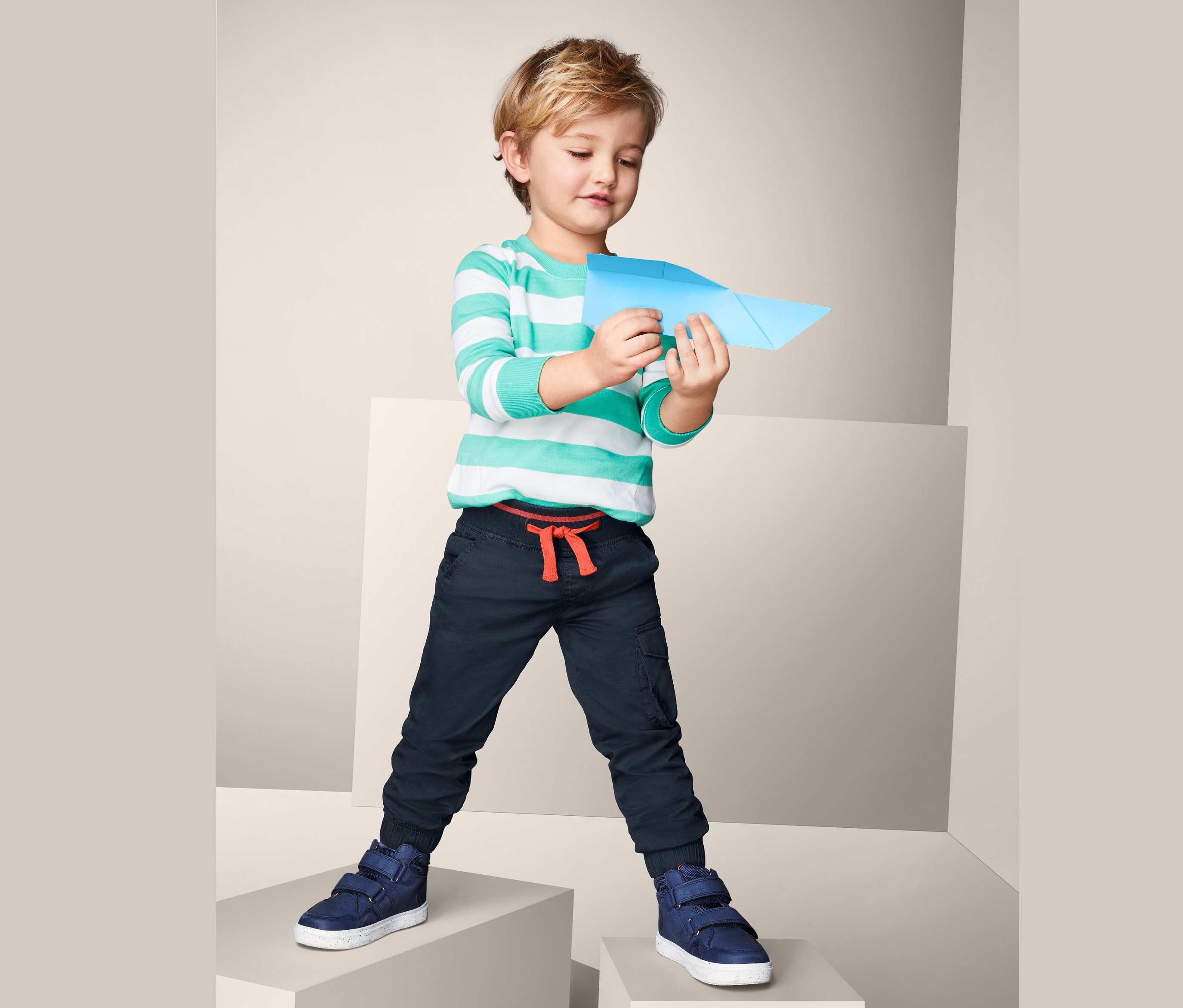 Chłopiec trzyma papierowy samolot i ma na sobie bawełniane spodnie na gumce.