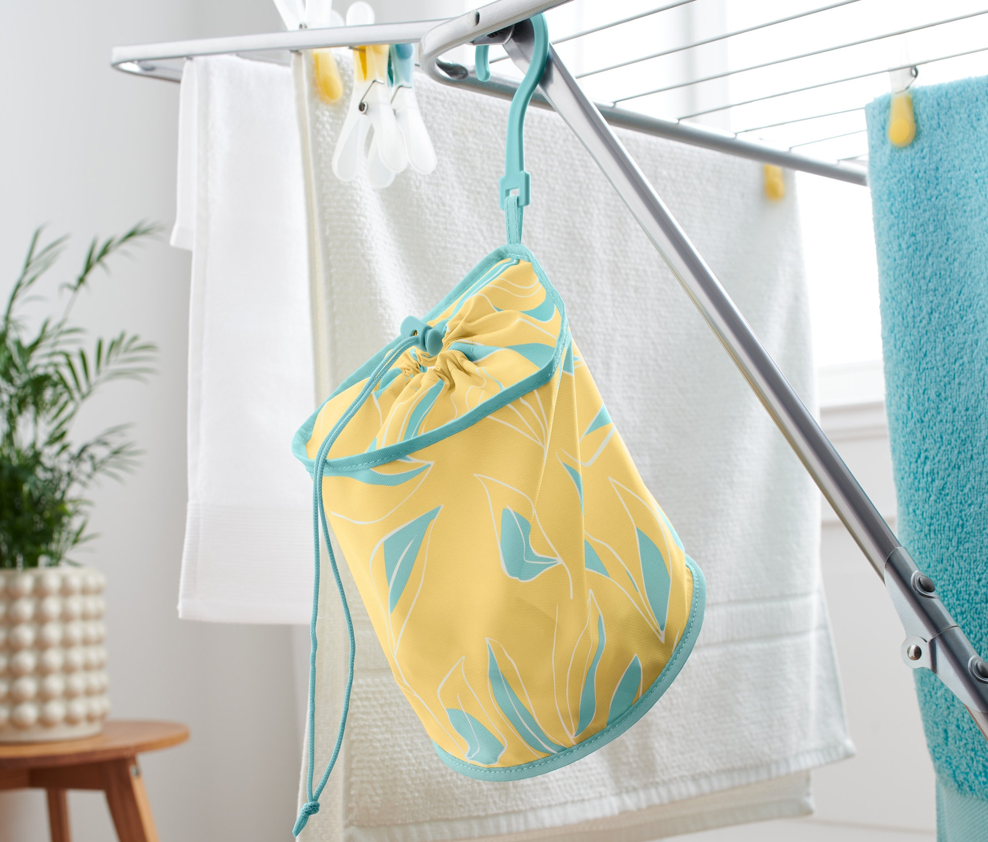 Żółty worek na klamerki do bielizny z niebieskim obszyciem wisi na suszarce do ubrań.
