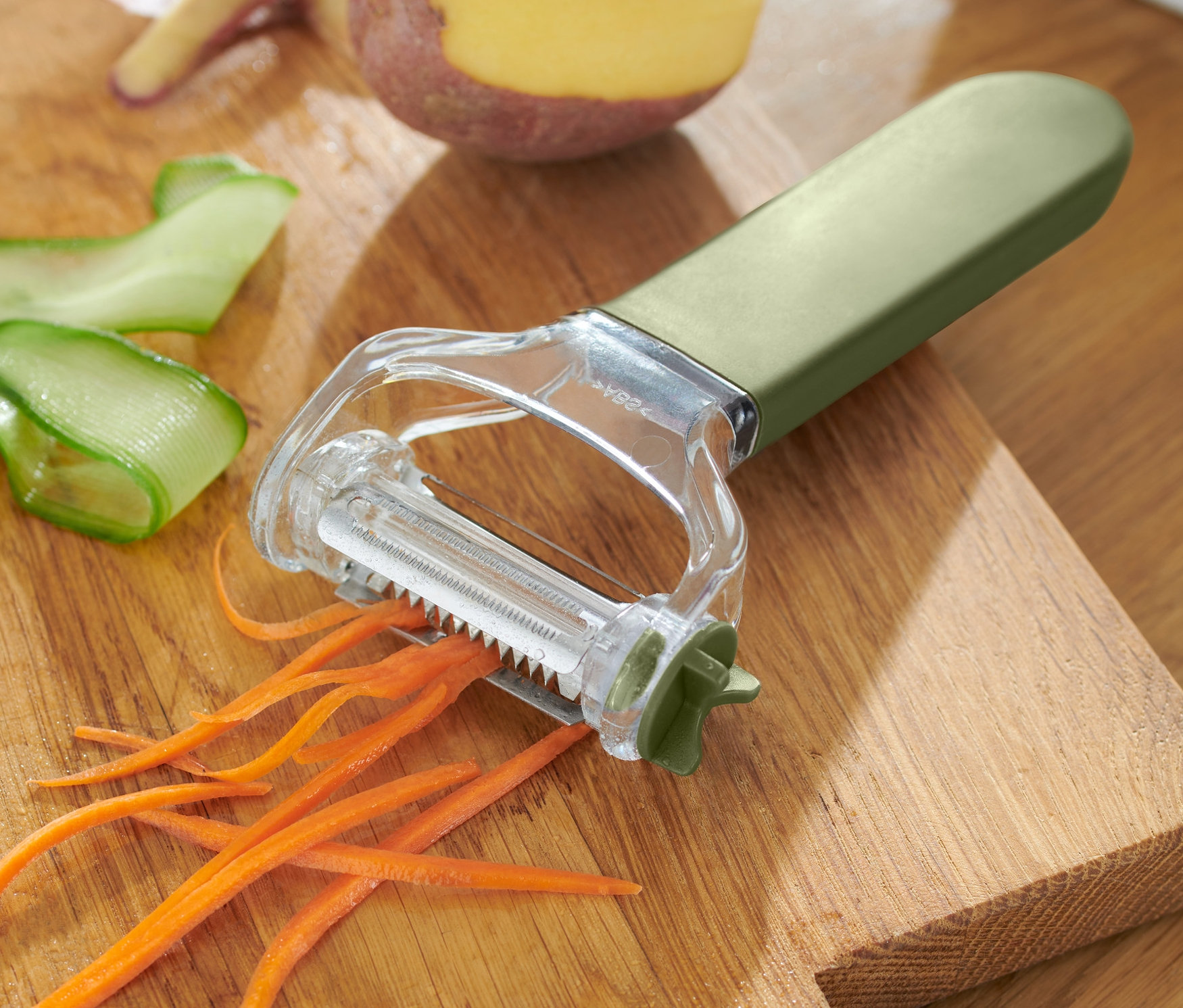 Obieraczka uniwersalna 3 w 1 leży na drewnianej desce do krojenia z resztkami marchwi, ogórka i ziemniaka.