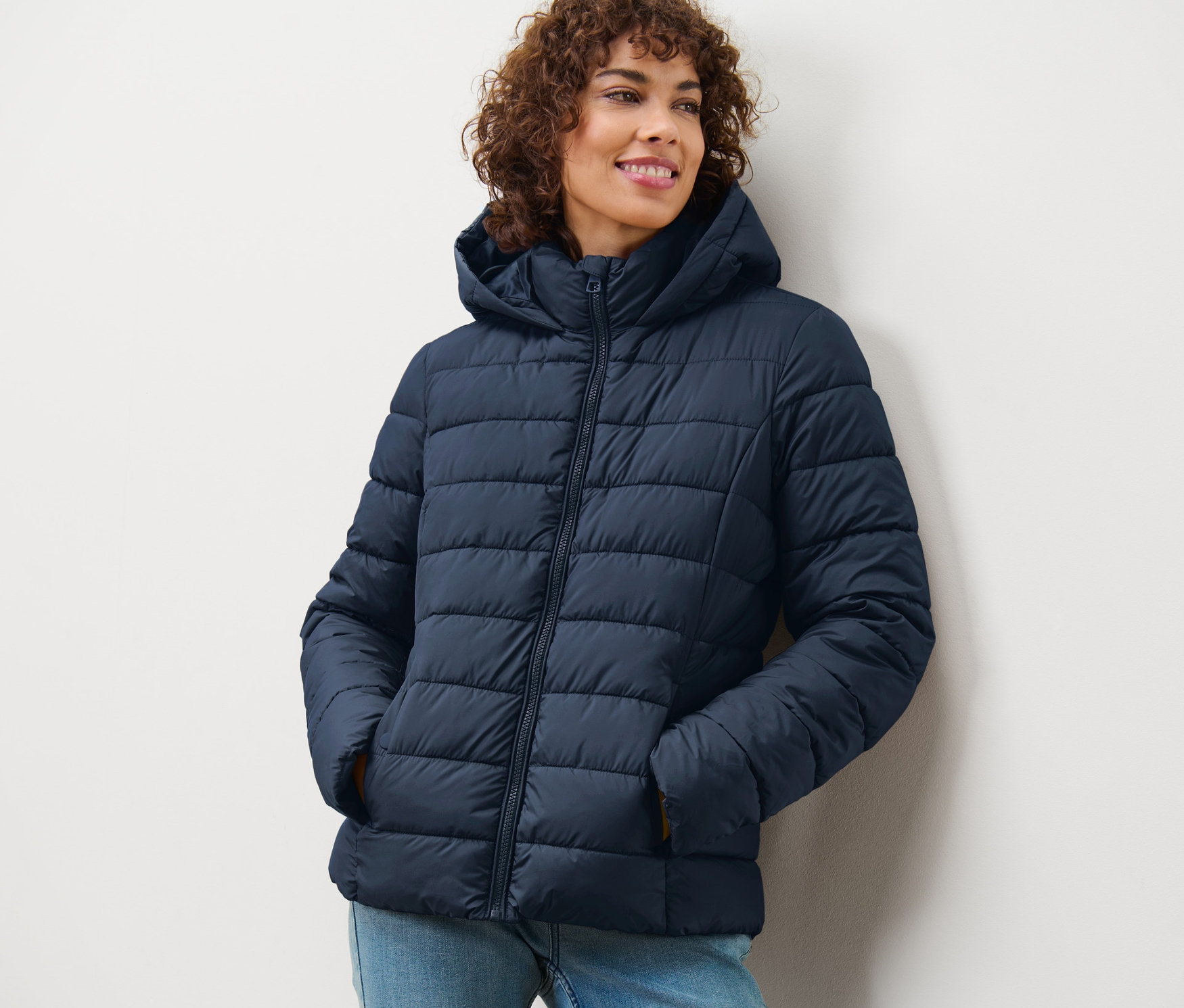Uśmiechnięta kobieta w granatowej kurtce pikowanej z kapturem.