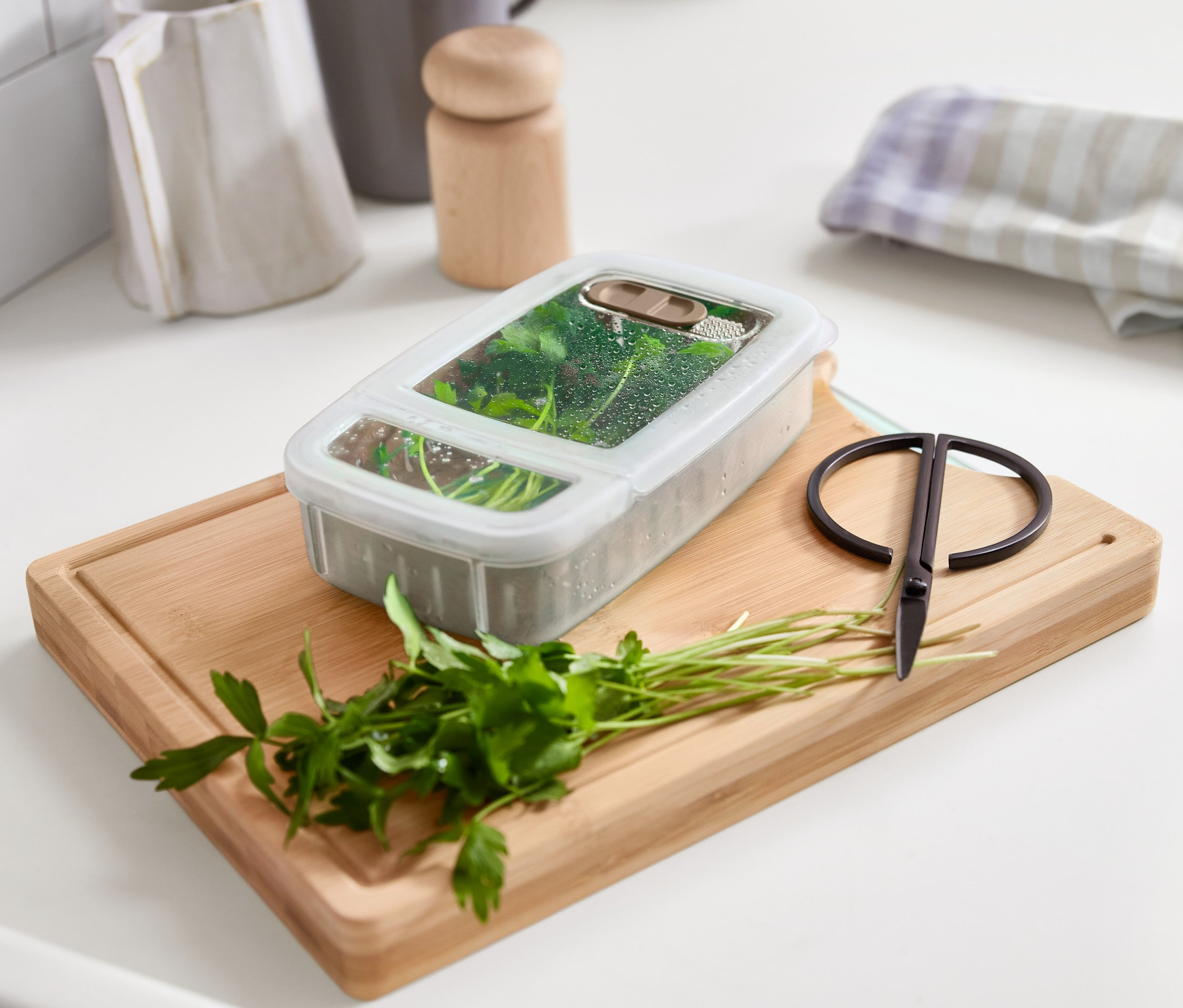 Pojemnik spożywczy na zioła leży na desce do krojenia z natką pietruszki i nożyczkami.