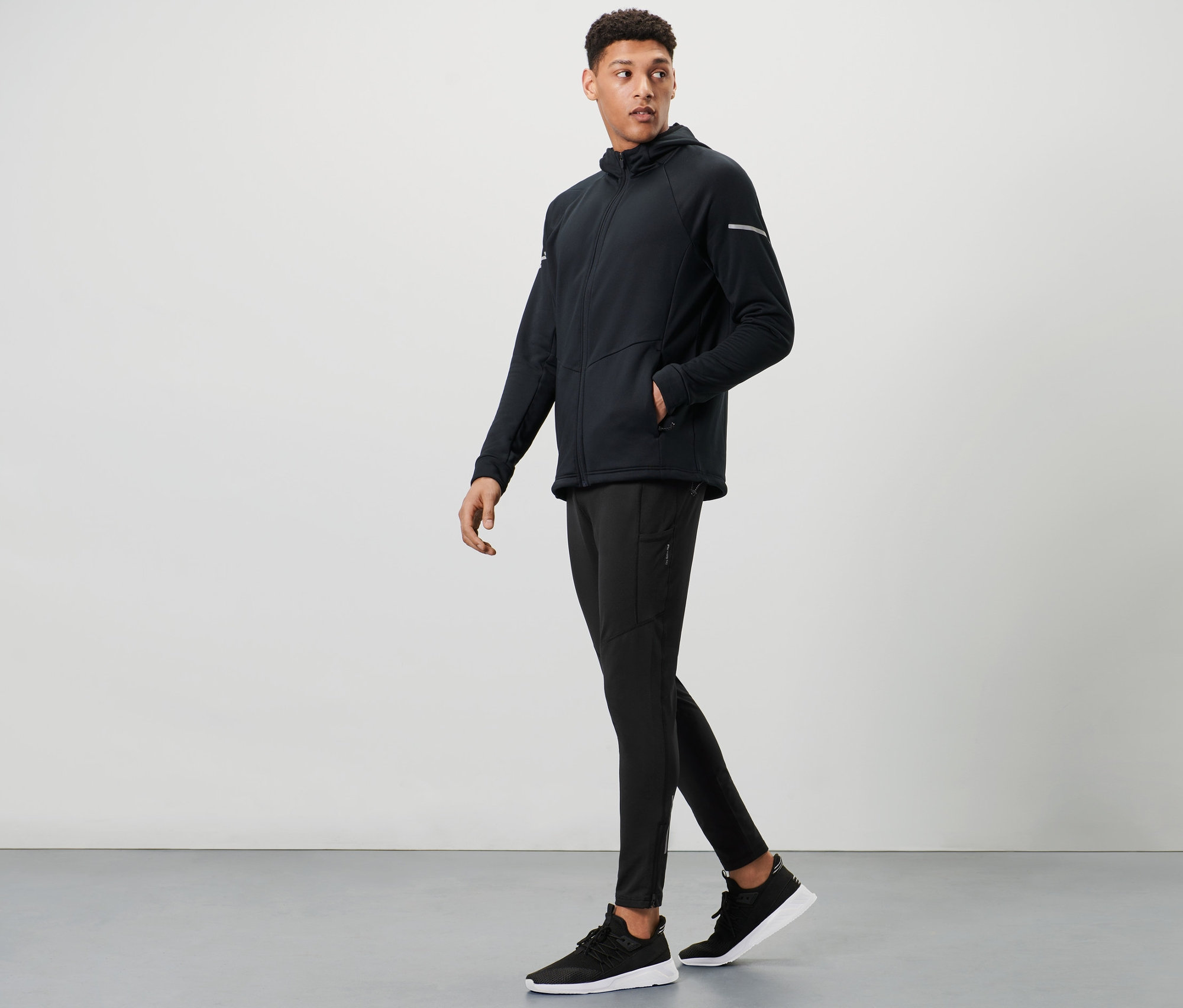 Mężczyzna idzie, ubrany w czarne legginsy termoaktywne i kurtkę.