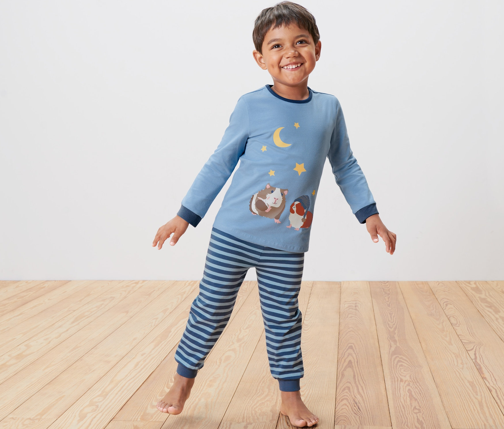 Chłopiec stoi i ma na sobie niebieską piżamę dziecięcą z motywem świnek morskich.