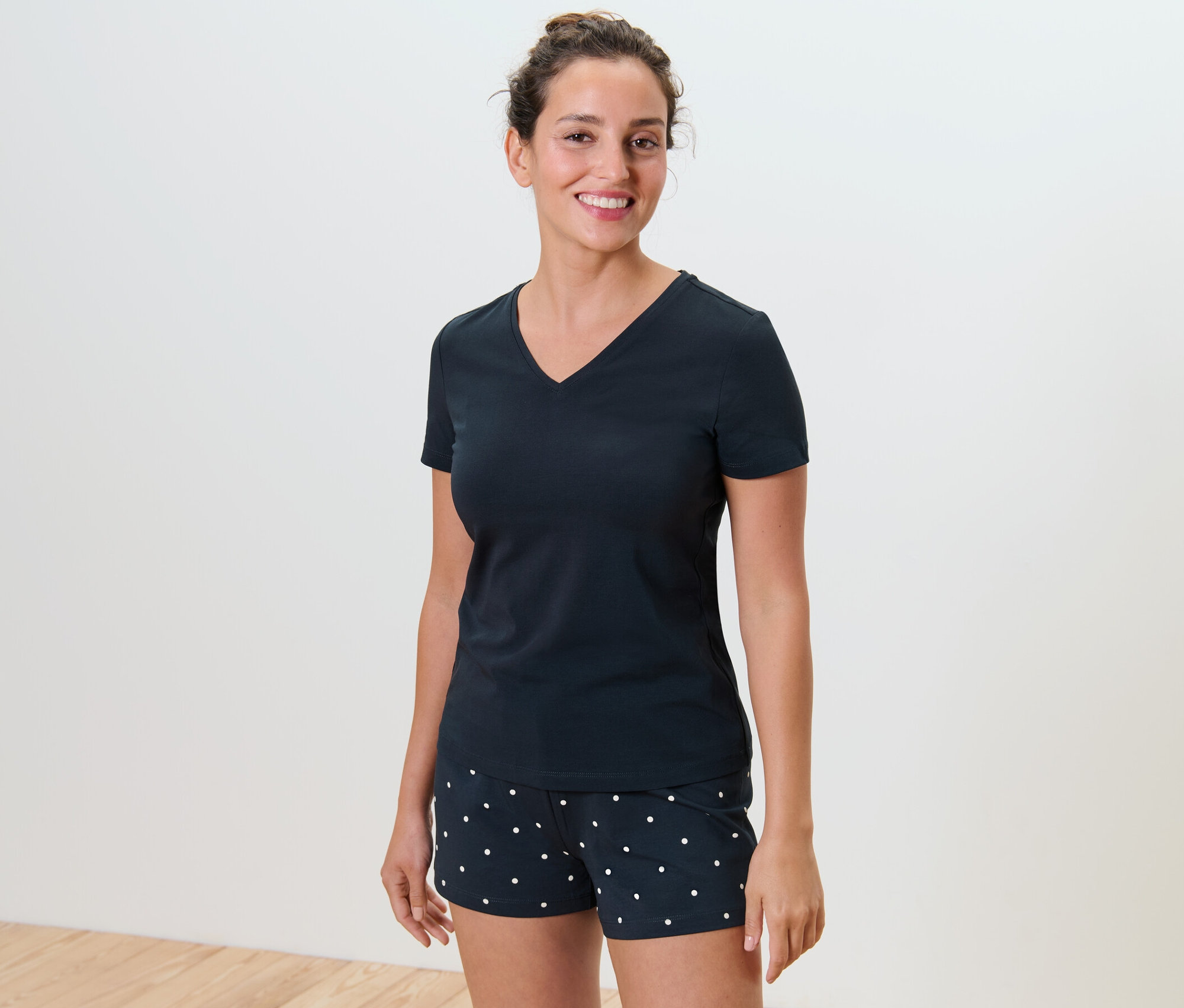 Uśmiechnięta kobieta ma na sobie piżamę z krótkimi spodenkami w kropki.