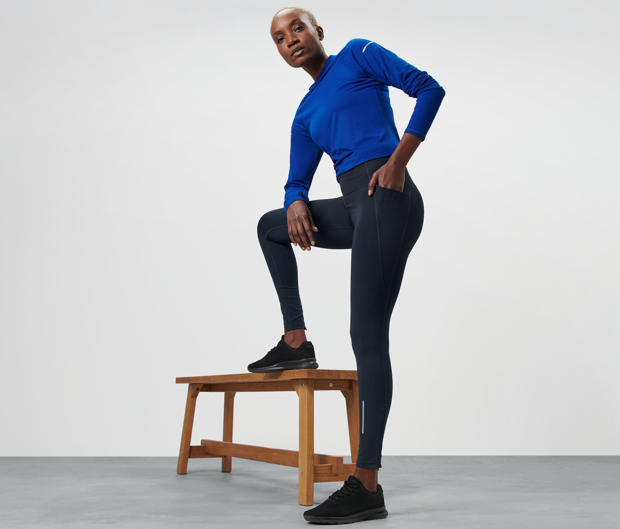 Kobieta pozuje na drewnianej ławce, ubrana w nieprzemakalne legginsy sportowe.