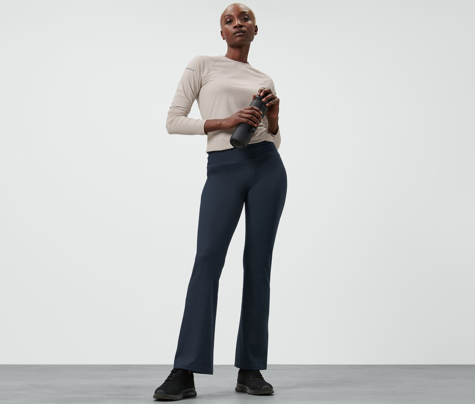 Kobieta trzyma butelkę wody i ma na sobie spodnie sportowe modelujące sylwetkę.