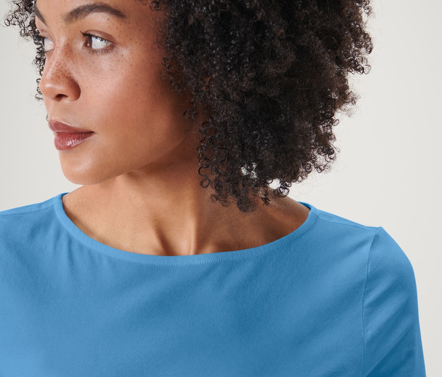 Portret kobiety z fryzurą afro, ubranej w jasnoniebieską bluzkę z rękawami o długości 3/4.