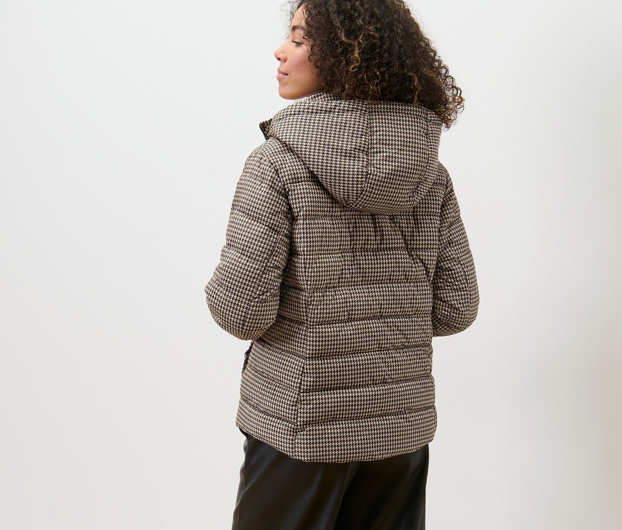 Kobieta ma na sobie pikowaną kurtkę z kapturem w pepitkę.