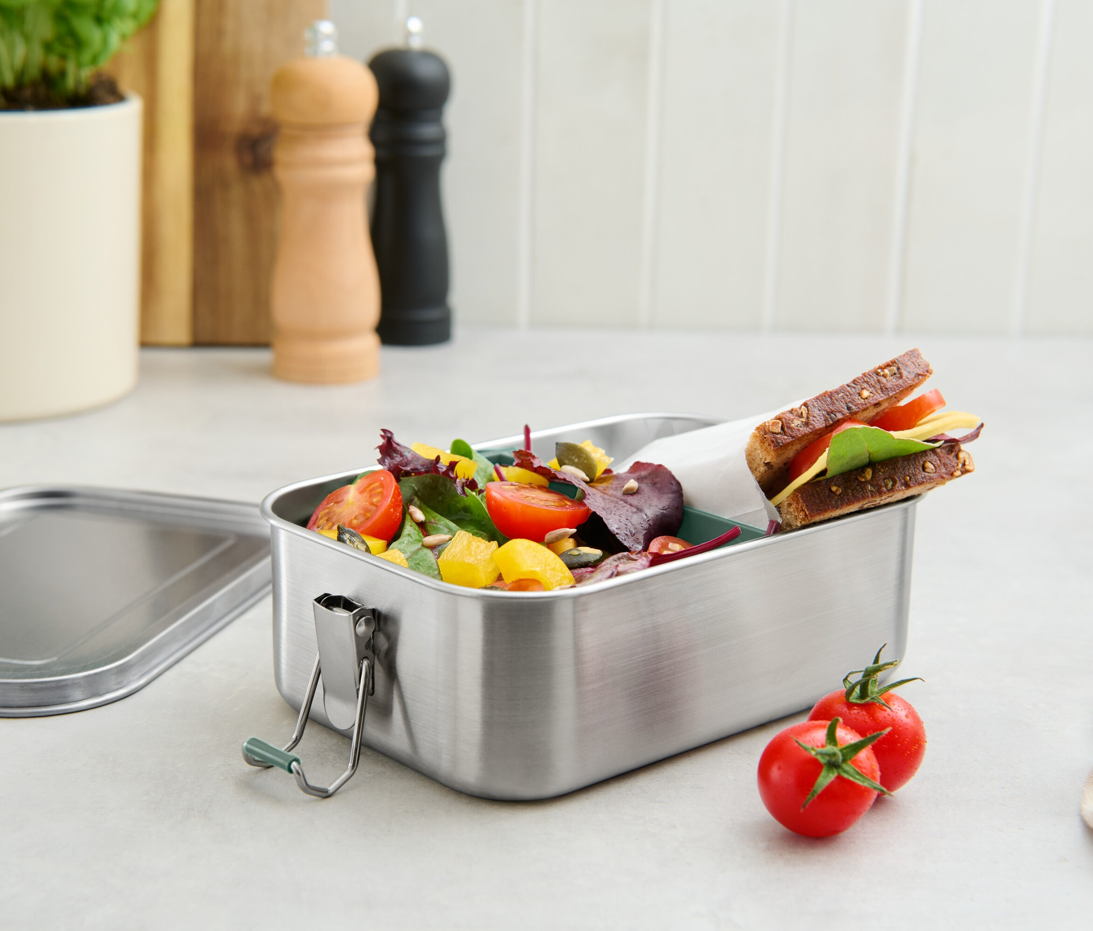 Pojemnik na lunch ze stali nierdzewnej wypełniony pomidorami, sałatą i kanapką.
