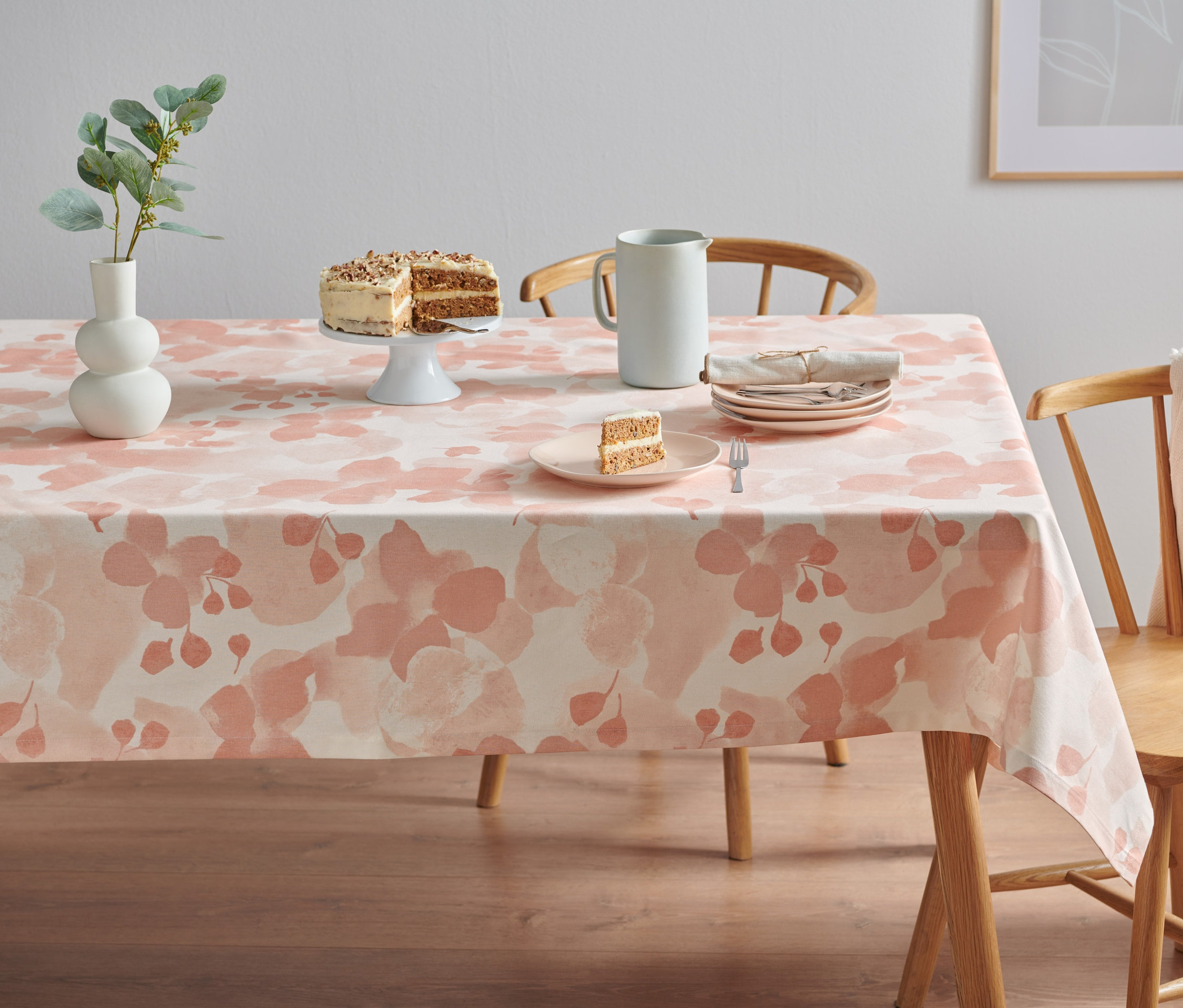 Na stole leży obrus o wymiarach ok. 140 x 180 cm. Na obrusie leżą ciasto, talerze i wazon.