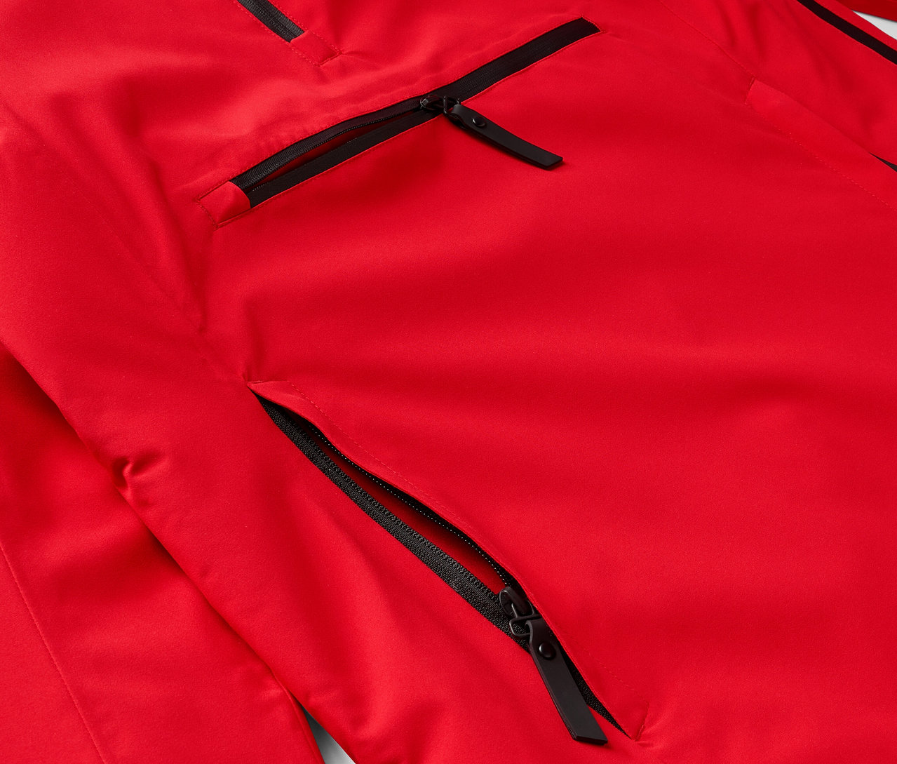 Detal czerwonej kurtki z czarnymi zamkami błyskawicznymi przy kieszeniach.