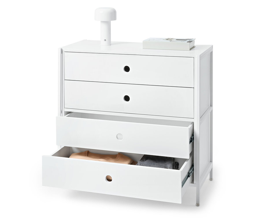 Biała komoda z trzema szufladami, z których dwie są otwarte i zawierają ubrania. Na komodzie stoi lampa i książka.