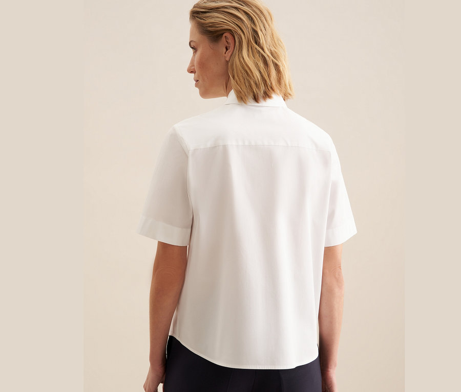 Kobieta tyłem do kamery ma na sobie białą koszulę z krótkim rękawem Seidensticker.