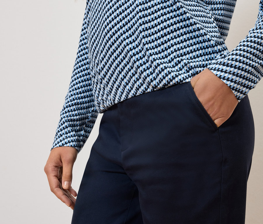 Częściowy widok osoby z ręką w kieszeni spodni i w niebiesko-białej bluzce.