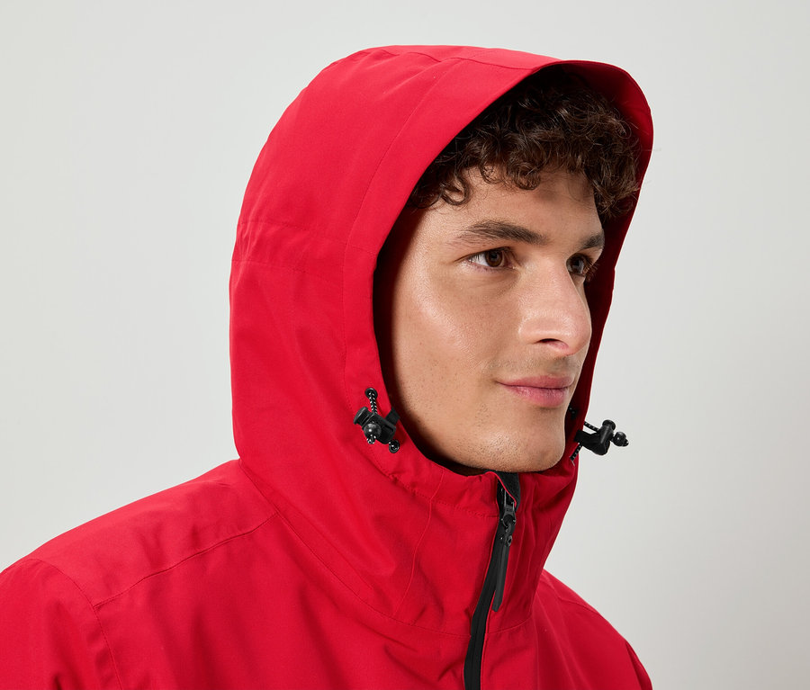 Mężczyzna z kręconymi włosami ma na sobie czerwoną kurtkę z kapturem.