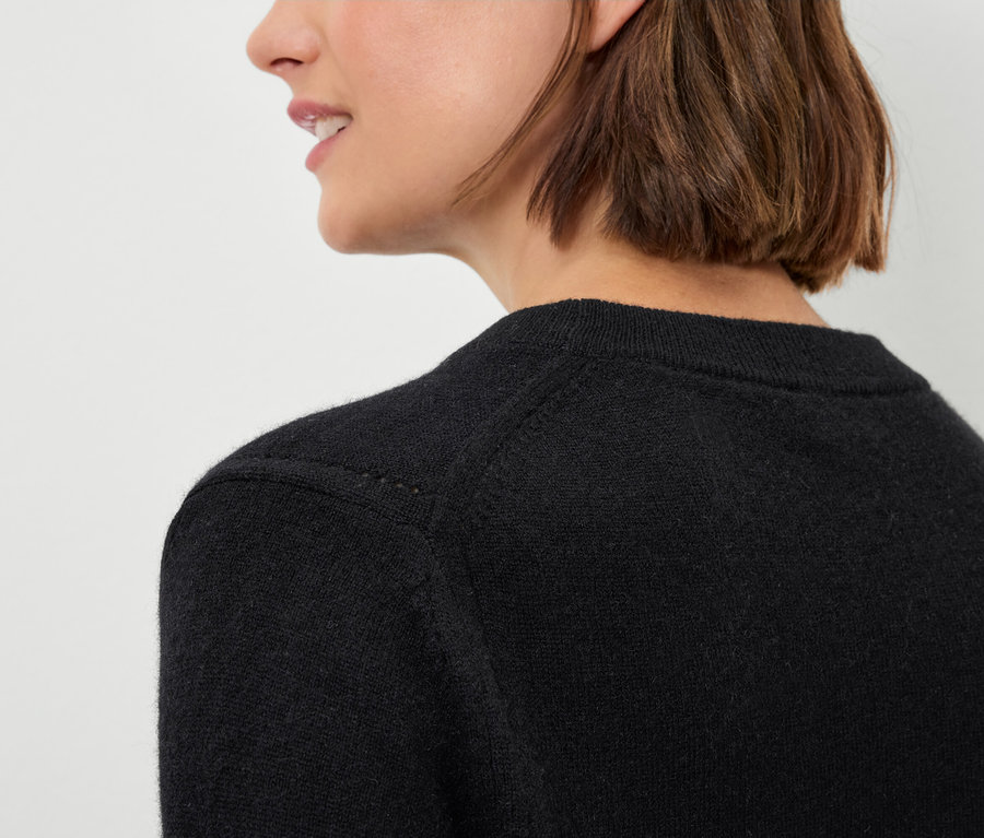 Detal czarnego damskiego swetra na kobiecie z brązowymi włosami.