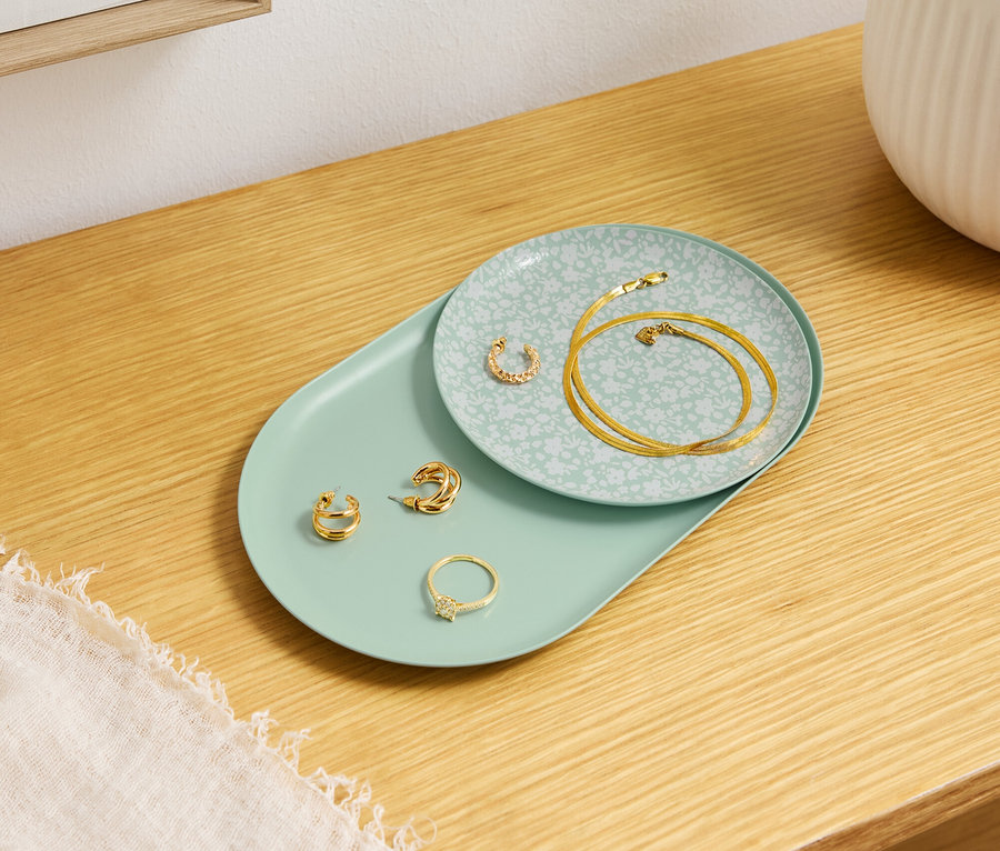 Złota biżuteria leży na ozdobnych talerzach na drewnianym stole.