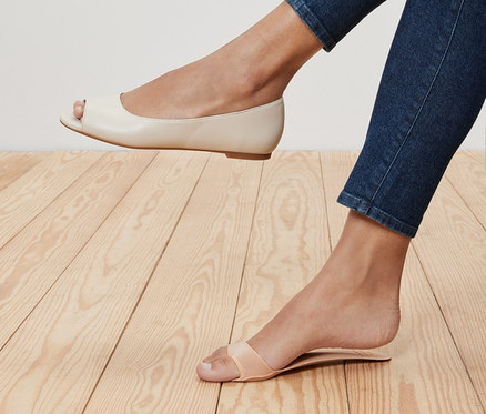 Nogi kobiety w dżinsach, jedna noga w kremowych balerinach peep toe, druga w sandałach z paskami. Wkładki do butów z wyściółką, 1 para, znajduje się w sandałach.