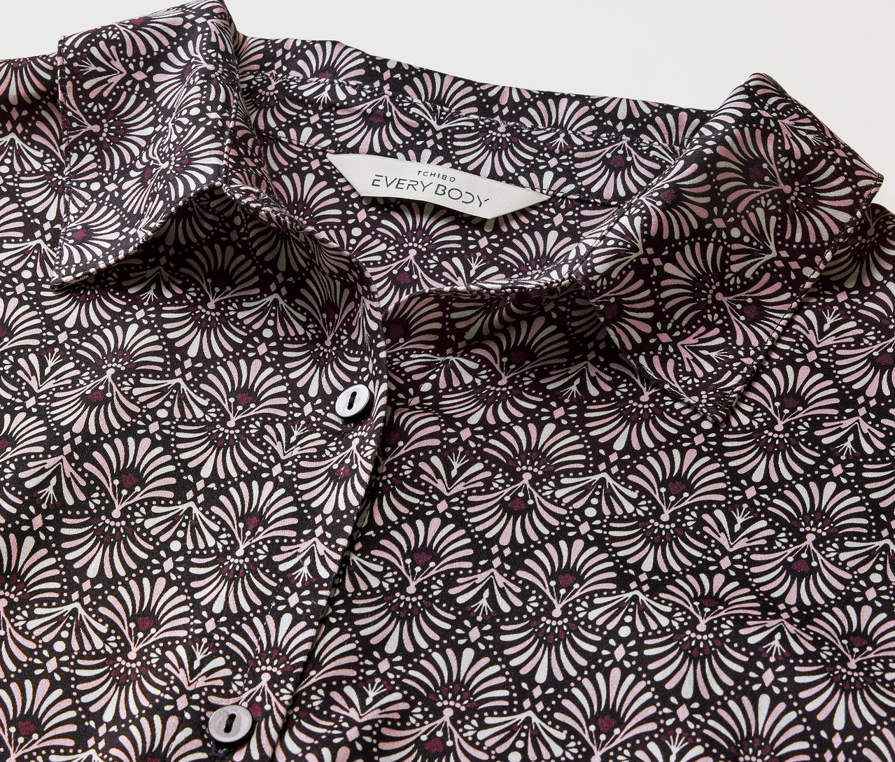 Zbliżenie tkanej koszuli nocnej z czarno-białym kwiatowym wzorem i guzikami.