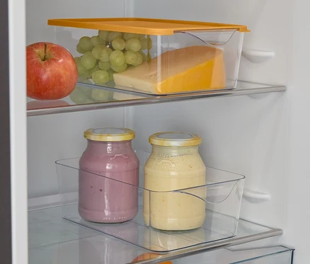 Otwarta lodówka z jabłkiem, winogronami, serem, dwoma szklankami smoothie, pomarańczą i limonkami.
