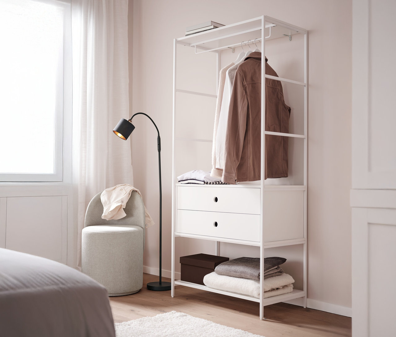 Obrotowy fotel z oparciem stoi obok białej garderoby „KLAAR” z 2 szufladami w sypialni.