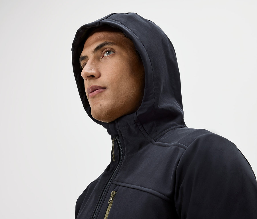 Portret mężczyzny w bluzie z kapturem i kurtce na zamek błyskawiczny, patrzącego w górę na białym tle.