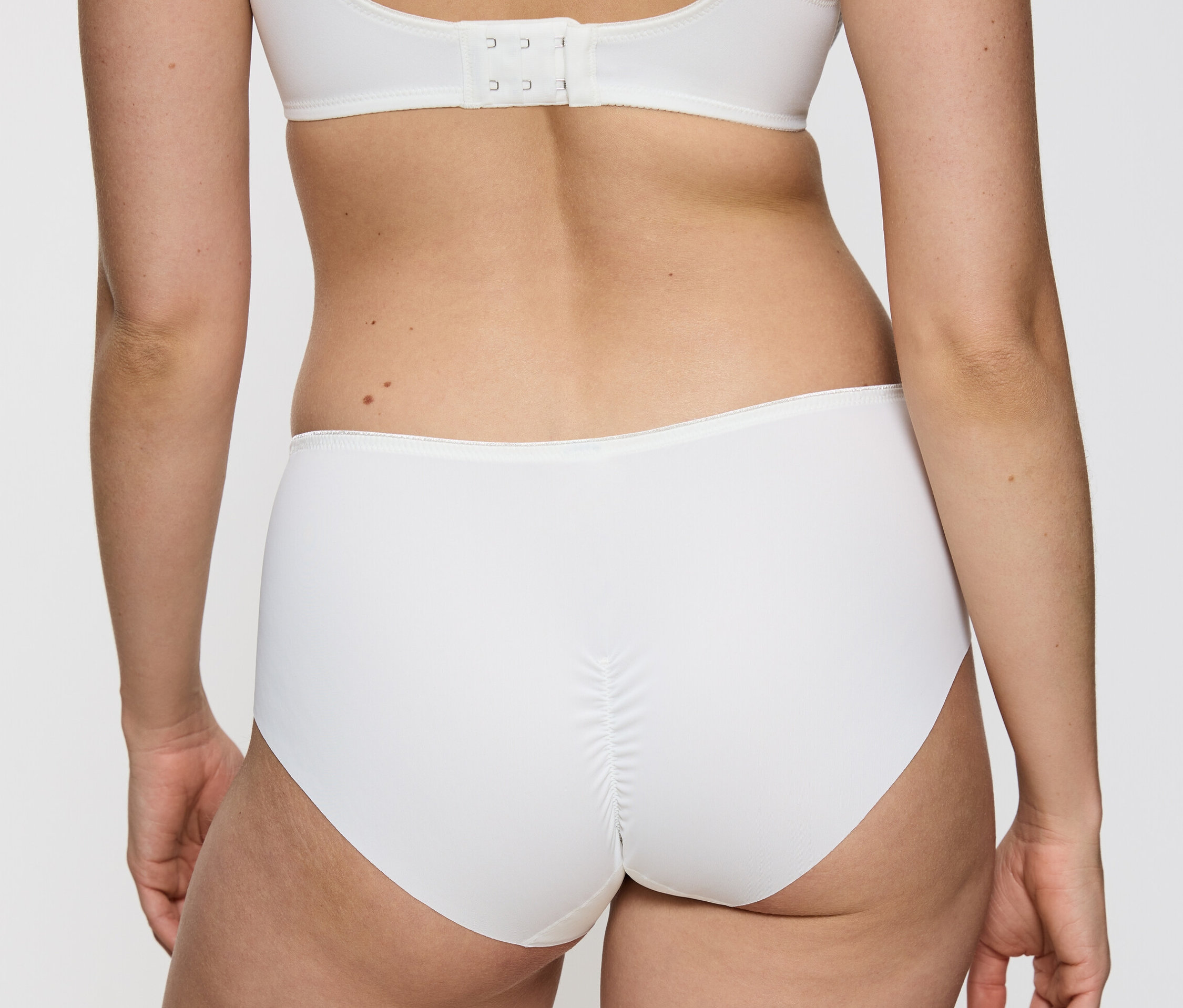 Widok z tyłu kobiety ubranej w białe figi typu hipster Triumph Essential „Minimizer Hipster X”, Vanille i biały biustonosz.