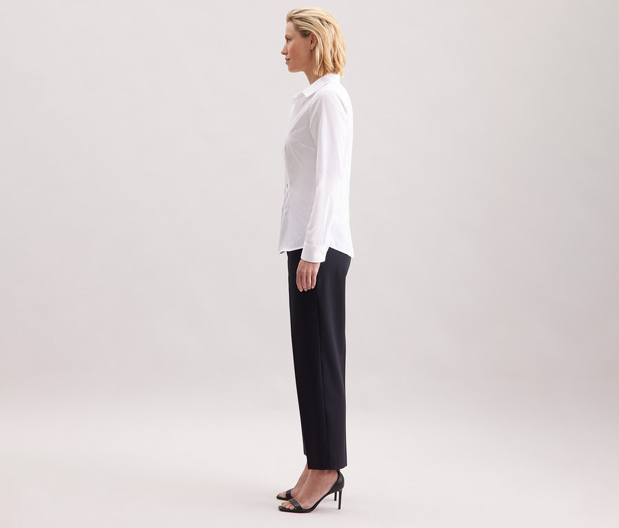 Profil kobiety noszącej białą bluzkę Seidensticker Slim Fit non iron, w połączeniu z ciemnymi spodniami i czarnymi butami na wysokim obcasie.