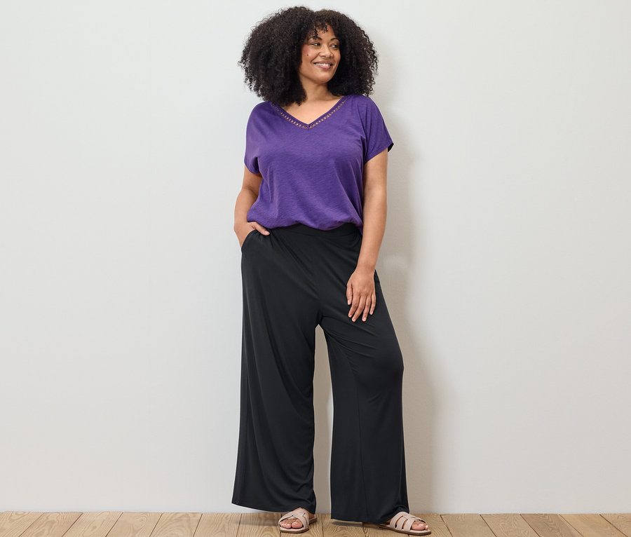 Kobieta pozuje w liliowej bluzce z mieszanki modalu i czarnych spodniach palazzo.