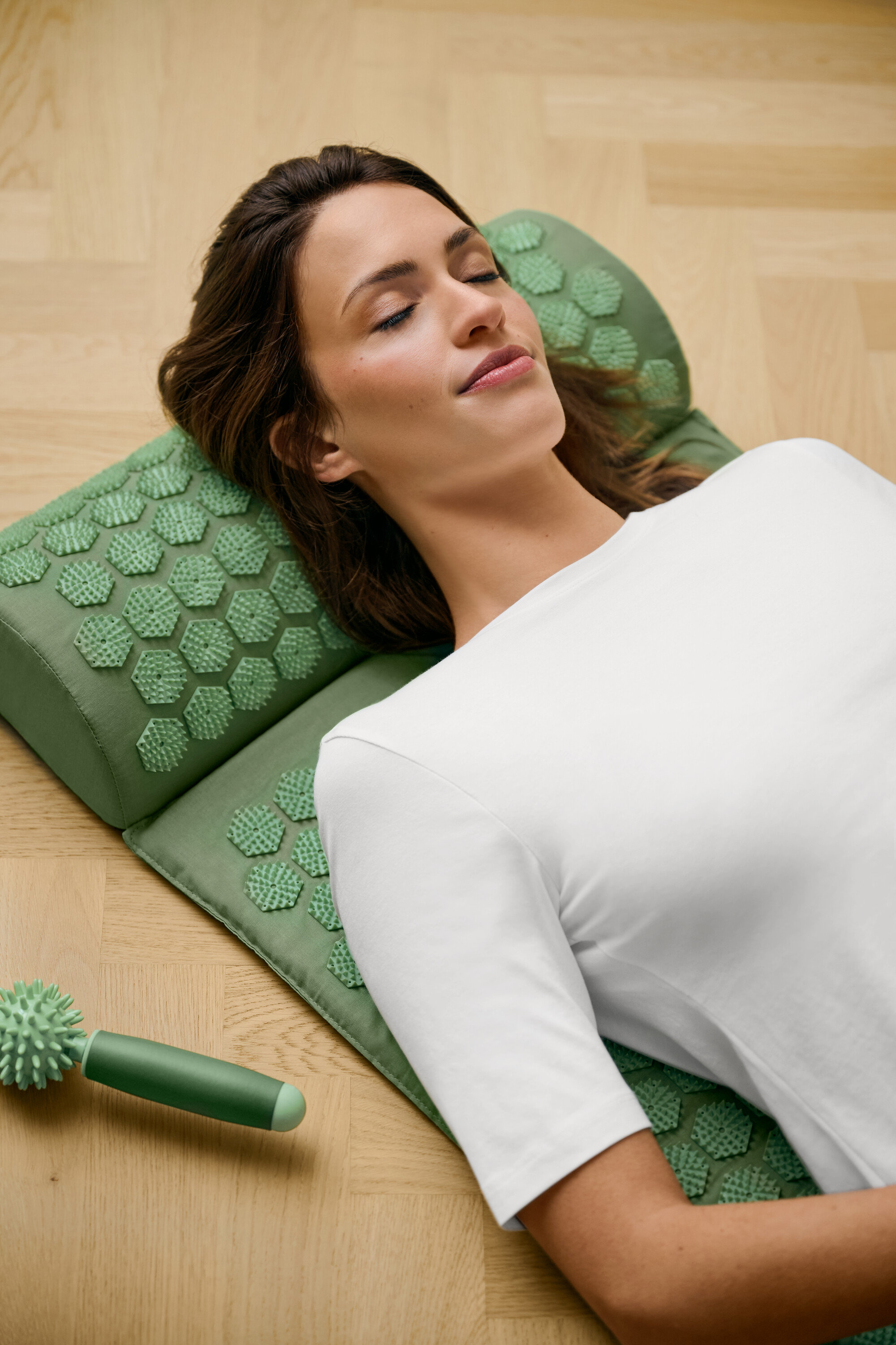 Kobieta leży na zielonej macie do akupresury i ma na sobie białą koszulkę z półrękawem.