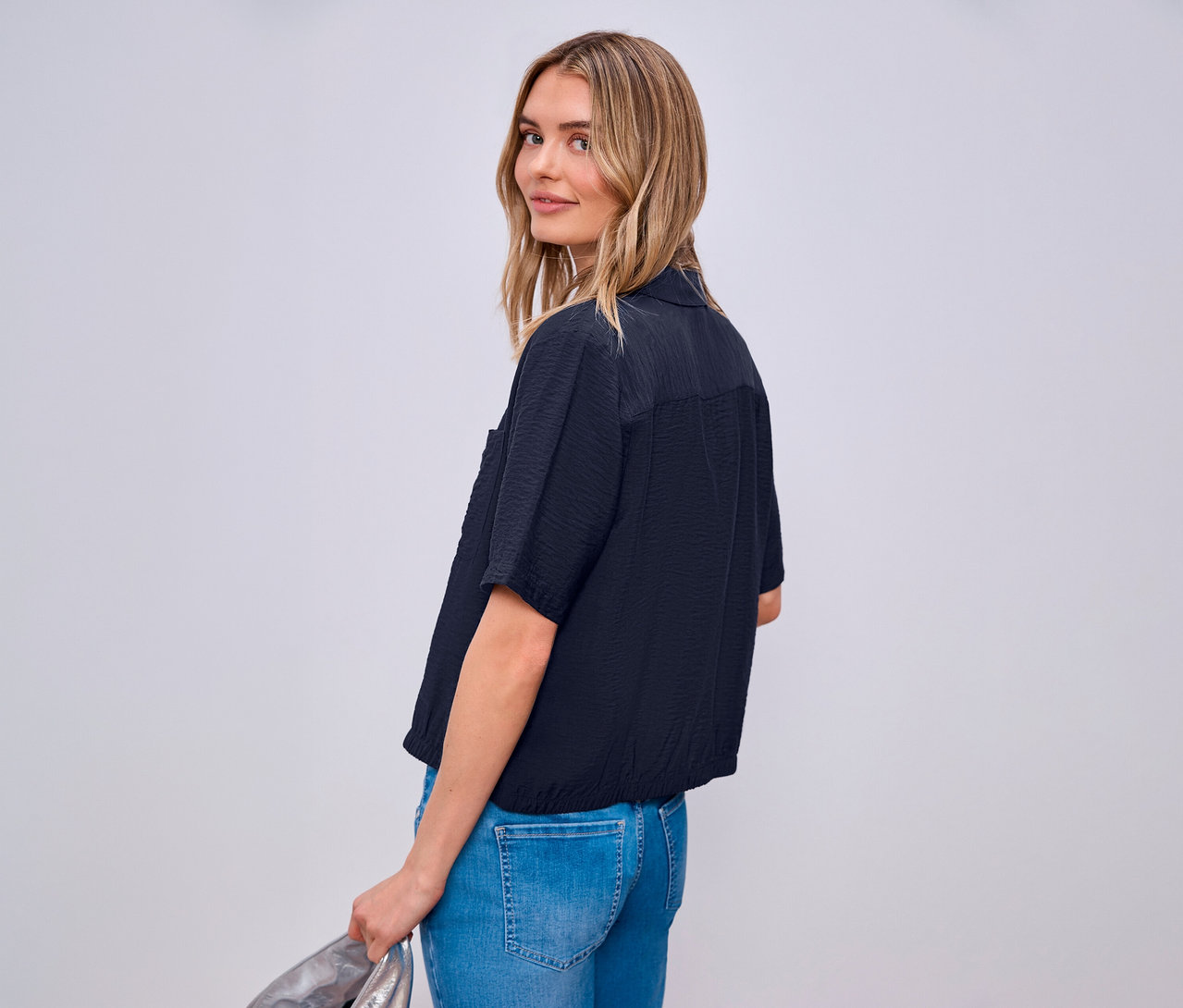 Kobieta patrzy przez ramię, ma na sobie dżinsy i koszulę Street One.